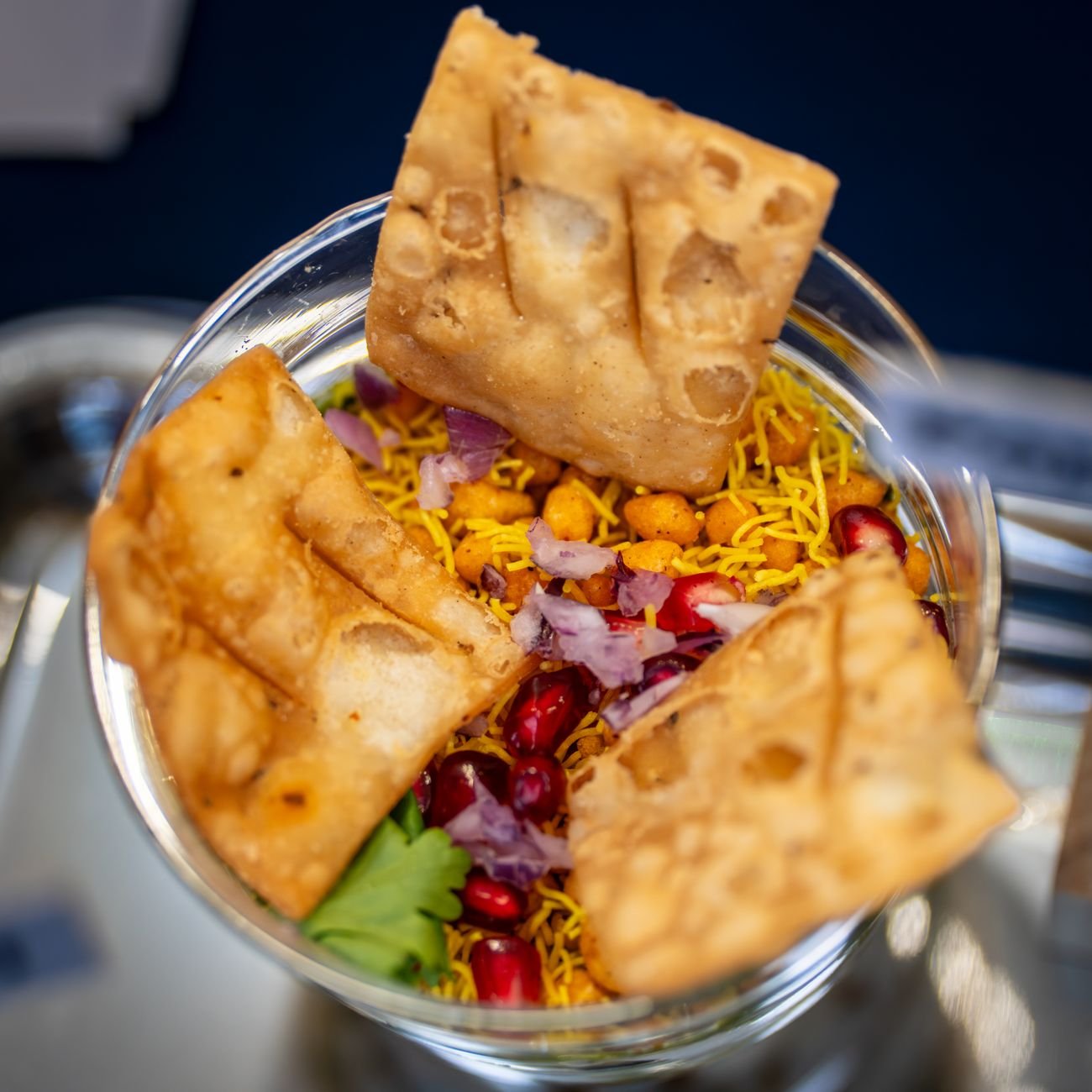 Vibrant Indian street food in a glass bowl topped with crispy papdi and pomegranate seeds